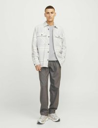 Langärmliges Karohemd in Grau und Weiß, mit zwei Brusttaschen, über einem hellgrauen Sweatshirt getragen, kombiniert mit grauen Hosen und Turnschuhen.