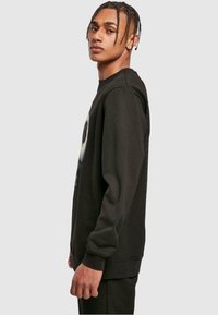 Black sweatshirt with long sleeves, round neckline, featuring a graphic design on the front, made of soft fabric with ribbed cuffs and hem.