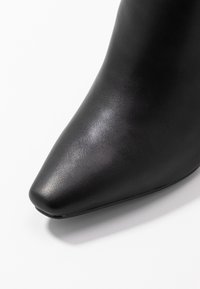 Schwarze Lederstiefel mit spitzem Fuß, glatter Textur und subtiler Glanz auf einem weißen Hintergrund.