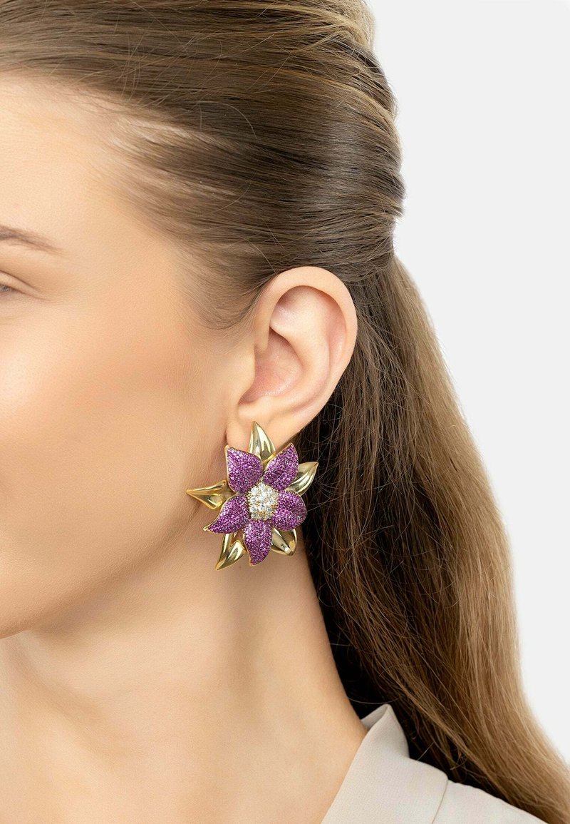 Gold-tone flower earrings with purple glitter petals and a central white gem. Features leaf-like accents. Shape resembles a blooming flower.