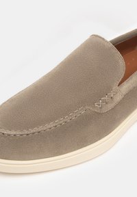 Scarpa slip-on in suede beige con una texture liscia, caratterizzata da cuciture tono su tono e una suola in gomma color crema. Accentuata da cuciture decorative.