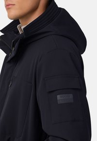 Mornarska vetrovka s teksturirano kapuco, zadrgo spredaj in logotipom na rokavu. Ima mehko, gladko izbiro tkanine in praktične žepe.