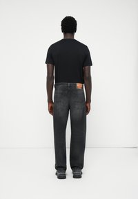 Svart t-skjorte og grå, litt falmede jeans med en synlig logo på baksiden av linningen. Jeansene har rett snitt og lommer.
