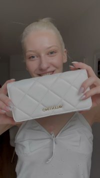 White quilted wallet with gold "Valentino" logo. Features rectangular shape, soft texture, and diagonal stitching pattern.