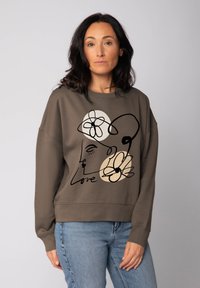Bruine sweatshirt met een relaxte pasvorm, met zwarte en beige lijntekeningen van een gezicht en bloemen, en het woord "Love" erop gedrukt.