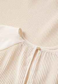 Lys beige top med vertikal ribbet tekstur, rund hals og knaplukning. Blødt stof med glat finish og detaljerede sømme.