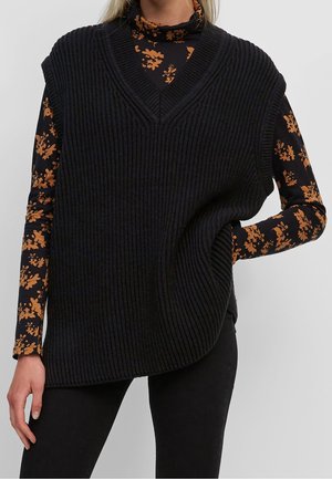 Schwarze gerippte, ärmellose Strickweste mit tiefem V-Ausschnitt und lockerer Passform, getragen über einem gemusterten Rollkragenpullover mit orangefarbenen Blumenmotiven.