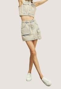 Denim crop top och matchande minikjol i ljusbeige, med knäppning, framficka och synliga sömmar. Vita sneakers.