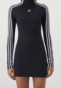Czarna sukienka z długim rękawem, z wysokim kołnierzem, z białymi akcentami w postaci trzech pasków na rękawach oraz małym białym logo Adidasa na piersi.