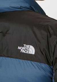 Black and blue insulated jacket featuring a checkered texture, with a white logo of "The North Face" on the chest area.