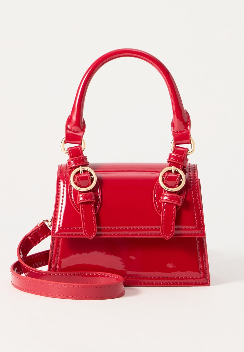 Sac à main en cuir verni rouge avec un design structuré, une anse ronde, des accents en métal doré et une bandoulière amovible.