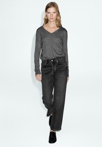 Top grigio a maniche lunghe e scollatura a V abbinato a jeans neri di denim a vita alta. I jeans hanno un taglio dritto e cuciture delle tasche anteriori ben visibili.