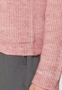 Rosa gestrickter Pullover mit einem strukturierten Muster, gerippten Bündchen und Saum. Verfügt über ein kleines Markenetikett am unteren Ende. Kombiniert mit grauen Hosen.