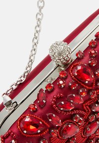 Pochette en satin rouge avec des ornements en bijoux rouges complexes, du matériel argenté et un fermoir orné de bijoux. Équipée d'une chaîne pour plus de polyvalence.