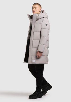 Cappotto puffer grigio chiaro con colletto alto, chiusura con zip e tasche laterali. Presenta una superficie trapuntata testurizzata e una toppa con logo sulla manica.