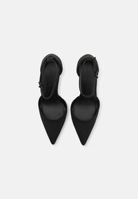 Svarta slingback-skor med spetsig tå, en slät mattyta och en tunn ankelsnodd, med en minimalistisk design och en elegant siluett.
