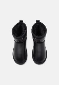 Bottes noires à la cheville avec un extérieur en cuir lisse, une doublure en fourrure douce et des œillets décoratifs en argent. Conçues avec des languettes pour un enfilage facile.