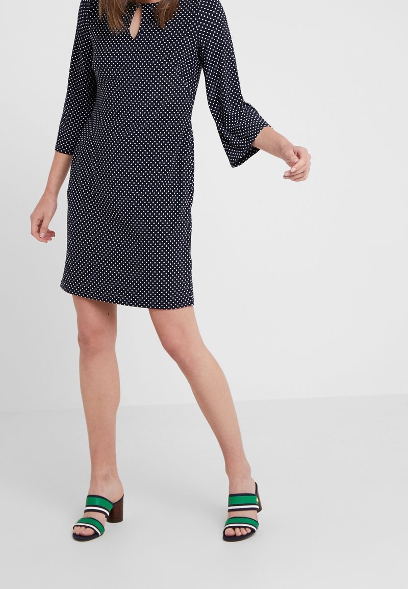 Námořnické šaty s bílými puntíky, výstřihem ve tvaru klíče, 3/4 zvonové rukávy. Vytvořeno s kombinací se zeleno-černými pruhovanými sandály na podpatku.