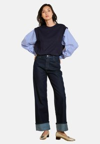Námorně modrý oversized svetr se pruhovanými modrými rukávy spárovaný s kalhotami širokého střihu z tmavého denimu, které mají ohrnuté manžety, a kovovými balerínami.