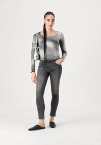 Haut à manches longues gris avec un effet dégradé et du texte à l'avant, associé à un jean skinny gris foncé, complété par des chaussures noires à enfiler et un sac argenté.