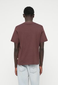 Bordeauxkleurig T-shirt met korte mouwen van zacht katoen, met een klassieke ronde hals en een rechte zoom. Draag het met lichtblauwe denim jeans.