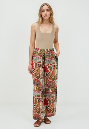 Débardeur beige côtelé associé à un pantalon large avec un motif géométrique coloré en rouge, vert et noir. Tissu texturé avec poches.