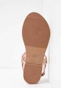 Roze gouden sandaal met een gestructureerde band, platte rubberen zool en geprinte details. Heeft een glad voetbed en een flexibele ontwerp.