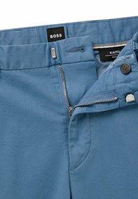 Blue slim-fit trousers made of smooth fabric. Features a metal zipper, button closure, and labels "BOSS" and "KAITO." Clean, minimalist design.