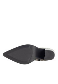 Zapato de tacón de punta afilada con un upper texturizado y con patrones en blanco y beige. Suela de goma negra con un acabado suave y un ligero arco.