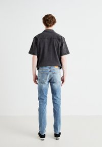 Camisa negra de manga corta, vaqueros azules descoloridos y zapatillas negras. La camisa presenta un diseño casual con cuello, mientras que los vaqueros tienen un corte ajustado.