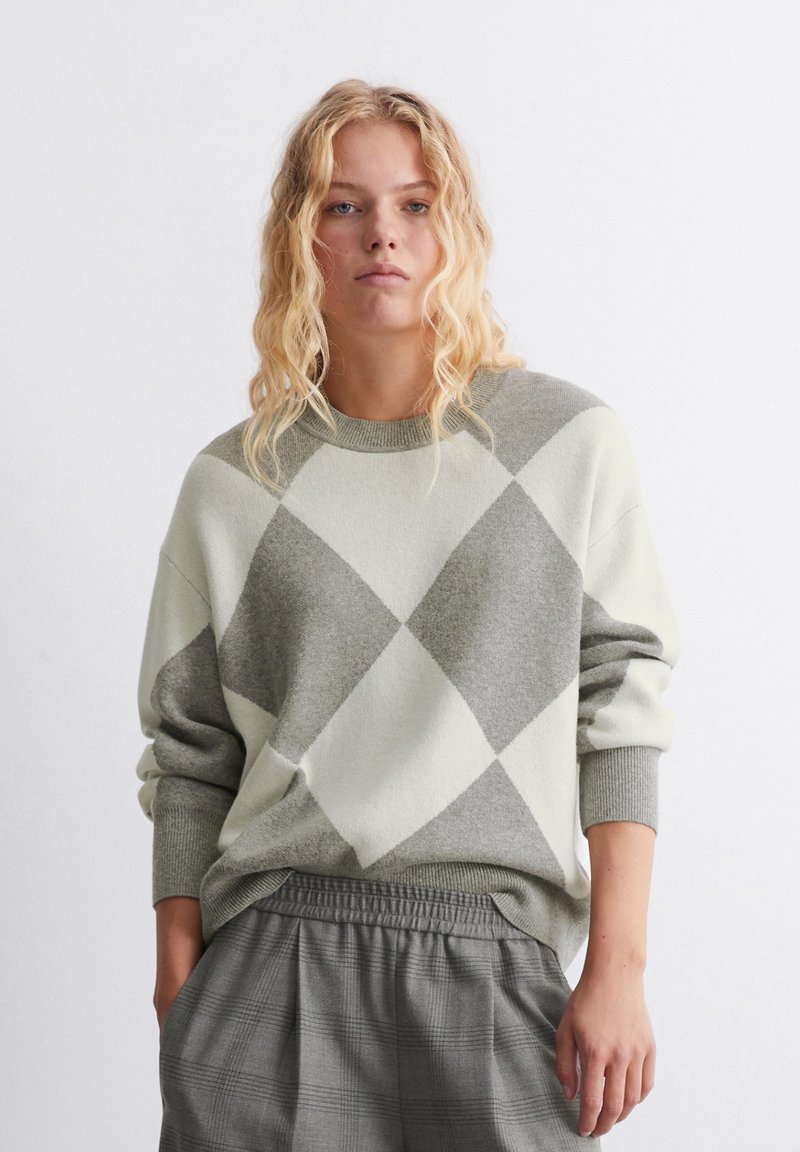 Hellgrüner und grauer Strickpullover im Argyle-Muster mit Rundhalsausschnitt, langen Ärmeln und lockerer Passform, kombiniert mit grauen Karohosen.