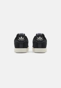 Sorte ruskinds sneakers med en hvid gummisål. Funktioner inkluderer kontrasterende syninger og et logo på hælen. Klassisk lavt design.