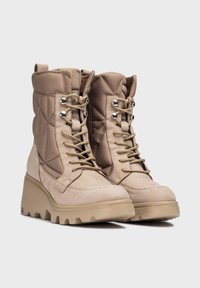 Botines beige con tejido acolchado, cordones en la parte delantera, ojales metálicos y una suela de cuña gruesa con acabado texturizado.