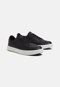 Zwarte leren sneakers met een gladde textuur, witte rubberen zool en vetersluiting. Kenmerkt subtiele branding aan de zijkant.