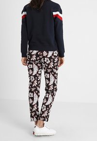 Maglione blu navy con strisce rosse e bianche sulle spalle, abbinato a pantaloni neri con motivo floreale e sneakers bianche.