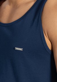 Top da donna in cotone morbido di colore blu navy, con scollatura rotonda e una piccola etichetta del marchio in argento sul petto. Design aderente.