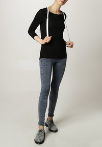 Czarna bluzka z długim rękawem, jasnoszare skinny jeans i teksturowane czarno-szare buty w wzory ze sznurowadłami. Białe paski zwisają z ramion.