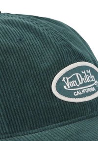 Casquette en velours côtelé vert présentant un patch ovale blanc avec le texte "Von Dutch CALIFORNIA". Surface texturée avec des stries visibles et des détails de couture.