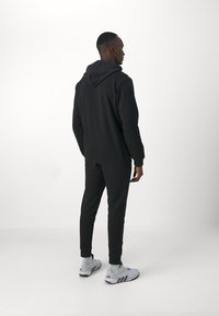 Sudadera negra con cordón, combinada con pantalones de chándal a juego. Zapatillas deportivas grises con acentos oscuros. Tejido suave de mezcla de algodón.