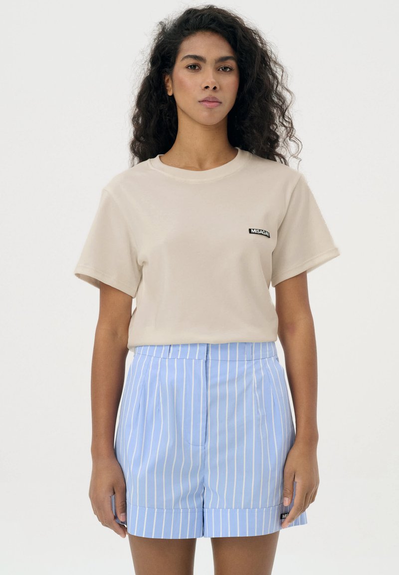 Beżowa bawełniana koszulka z krótkim rękawem i okrągłym dekoltem, z czarną naszywką z logo. W zestawie z niebieskimi spodniami w pionowe paski.