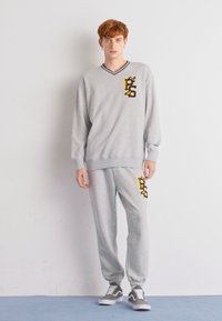 Grau Sweatshirt- und Jogginganzugset mit V-Ausschnitt, gerippten Bündchen und gelben grafischen Akzenten. Baumwollmaterial mit weicher Textur.