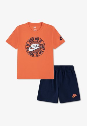 Camiseta naranja de manga corta de Nike con el logo "Just Do It" combinada con pantalones cortos de cintura elástica azul marino con un logo naranja de Nike.