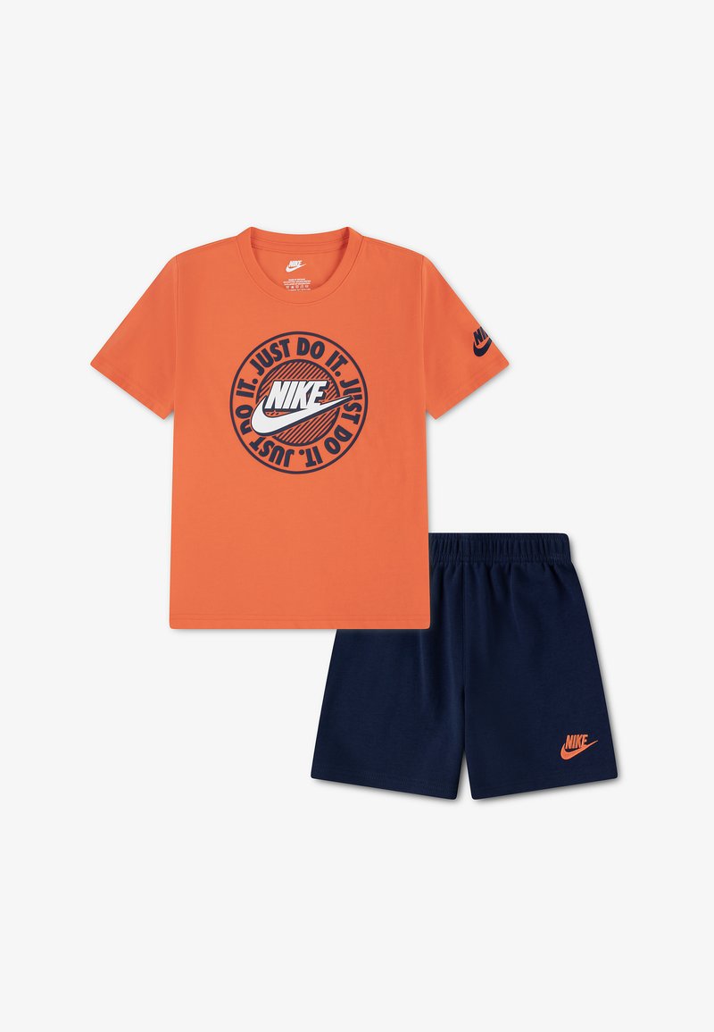 Πορτοκαλί κοντομάνικη μπλούζα Nike με το λογότυπο "Just Do It" σε συνδυασμό με σορτς με ναυτικό μπλε ελαστική μέση και πορτοκαλί λογότυπο Nike.