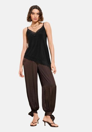 Melna krekliņa ar mežģīņu apdari, kopā ar brūnām, platu biksēm ar piesaistāmiem manžetēm, papildināts ar vairākslāņu kaklarotu un augstpapēžu kurpēm.