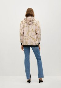 Jasnoróżowa kurtka z kapturem ozdobiona wzorem w złote łańcuchy, wykonana z gładkiego materiału, z czarnym obszyciem i prążkowanymi mankietami poniżej talii.