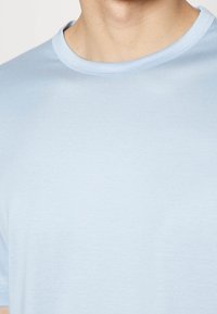 Světle modré bavlněné tričko s kulatým výstřihem a krátkými rukávy, které se vyznačuje hladkou texturou a minimalistickým designem.