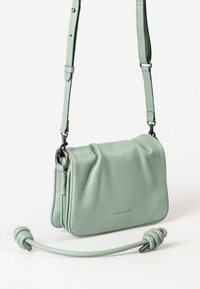 Kleine mintgroene leren schoudertas met verstelbare strap en aparte bovengreep met knoopuiteinden, staand tegen een witte achtergrond.