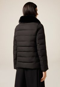 Schwarze Steppjacke mit Kunstpelzkragen, mit gesteppter Optik und leicht verkürzten Ärmeln, glatter Textur und zurückhaltender Silhouette.