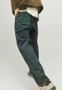 Tumedates denimis Relaxed fit teksad, millel on roheline tikand tagakotil. Kombineeritud heledate kingadega.