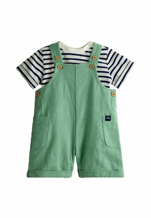 Salopette corta verde in cotone con tasche e bottoni di legno, indossata sopra una maglietta a righe bianche e blu navy a maniche corte per bambini piccoli.